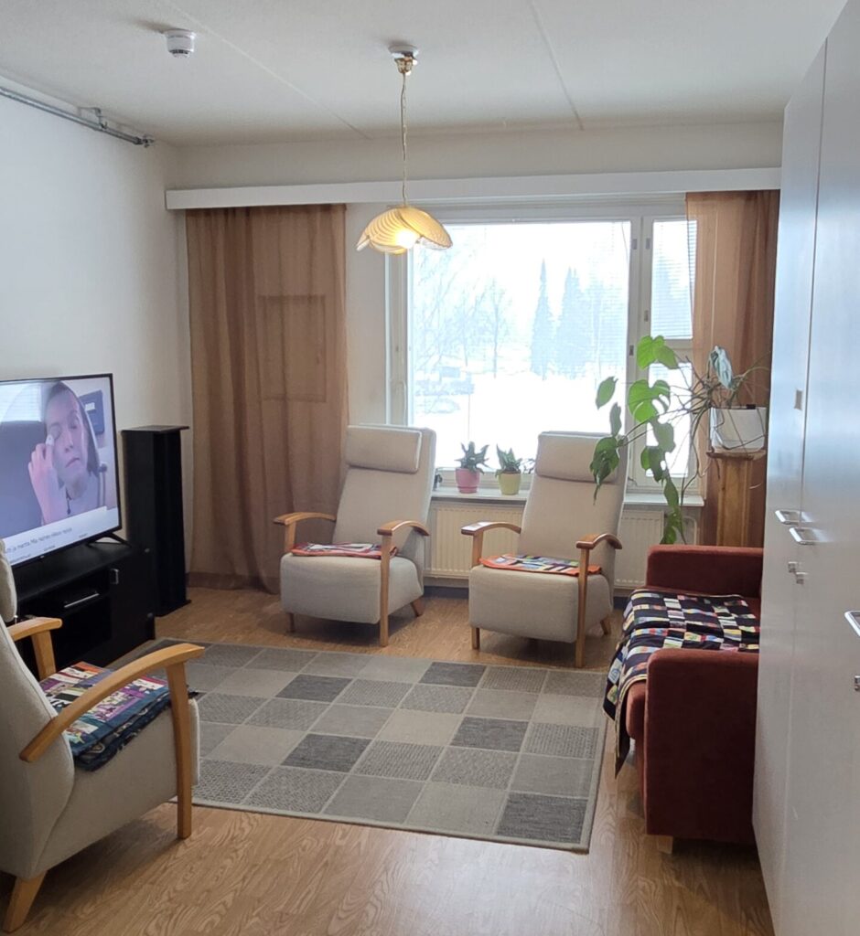 Ryhmäkodin viihtyisä oleskelutila, nojatuolit ja televisio.